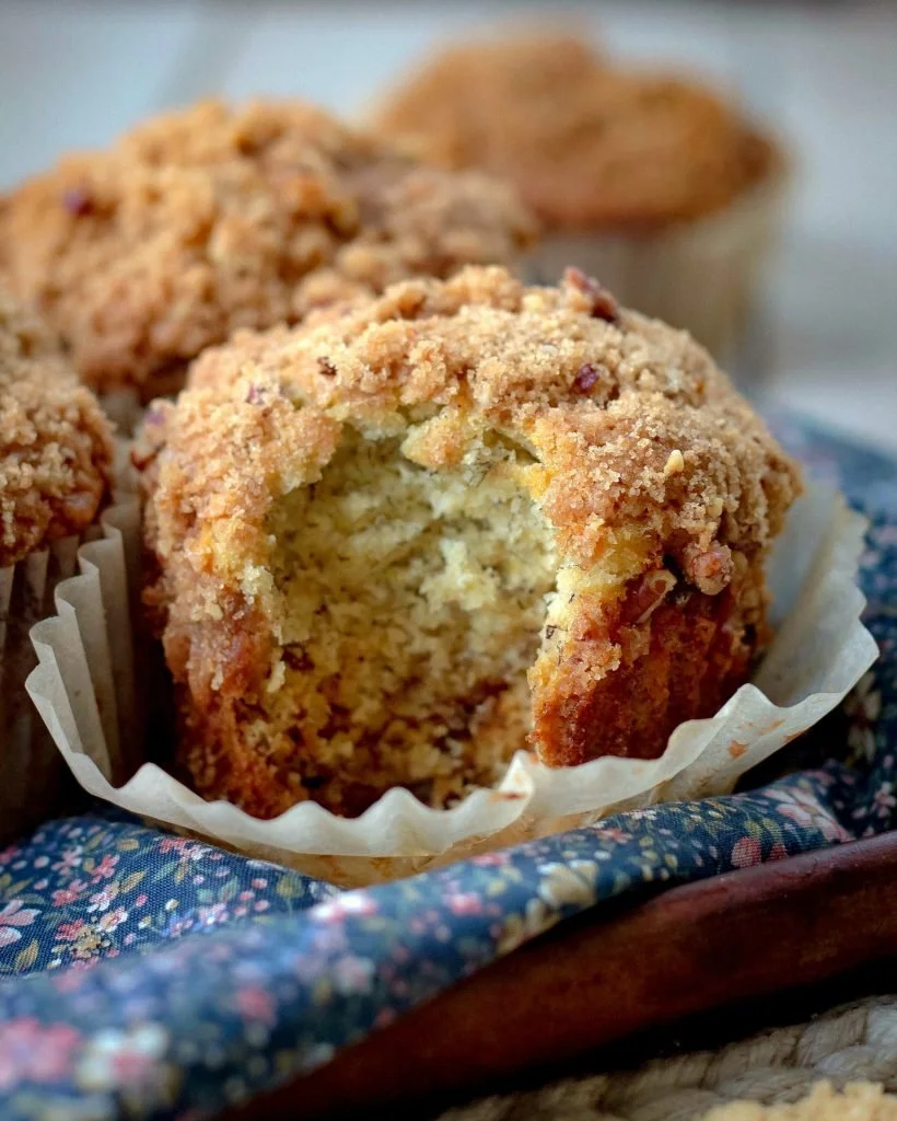 Delicious banana muffins topped with a crunchy crumb topping on a wooden table.