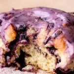 Freshly baked blueberry cinnamon rolls with icing on a wooden table