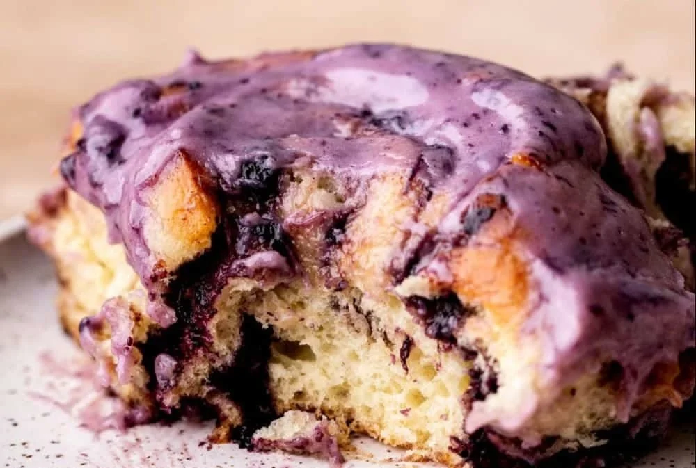 Freshly baked blueberry cinnamon rolls with icing on a wooden table