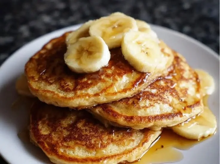 Delicious fluffy banana pancakes stacked on a plate, drizzled with syrup