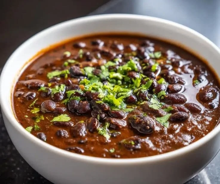 Bowl of hearty black bean soup garnished with cilantro and served with crusty bread.