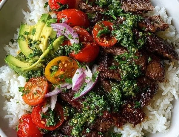 Skirt steak rice bowl with chimichurri sauce garnished with fresh herbs.