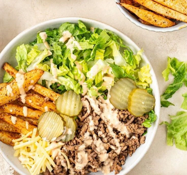 A vibrant burger bowl filled with fresh vegetables, grilled beef, and sauce