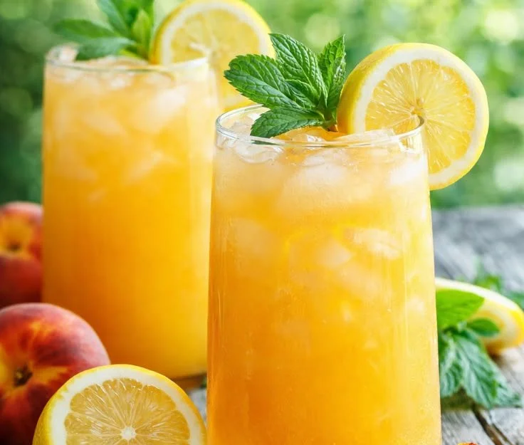 Homemade peach lemonade in a glass with fresh peaches and lemons