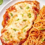 Baked Chicken Parmesan served with fresh herbs and marinara sauce on a plate