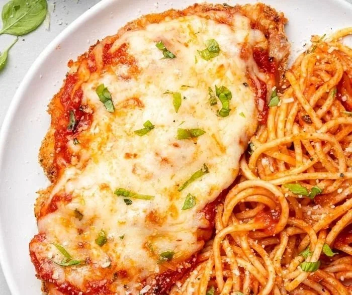 Baked Chicken Parmesan served with fresh herbs and marinara sauce on a plate
